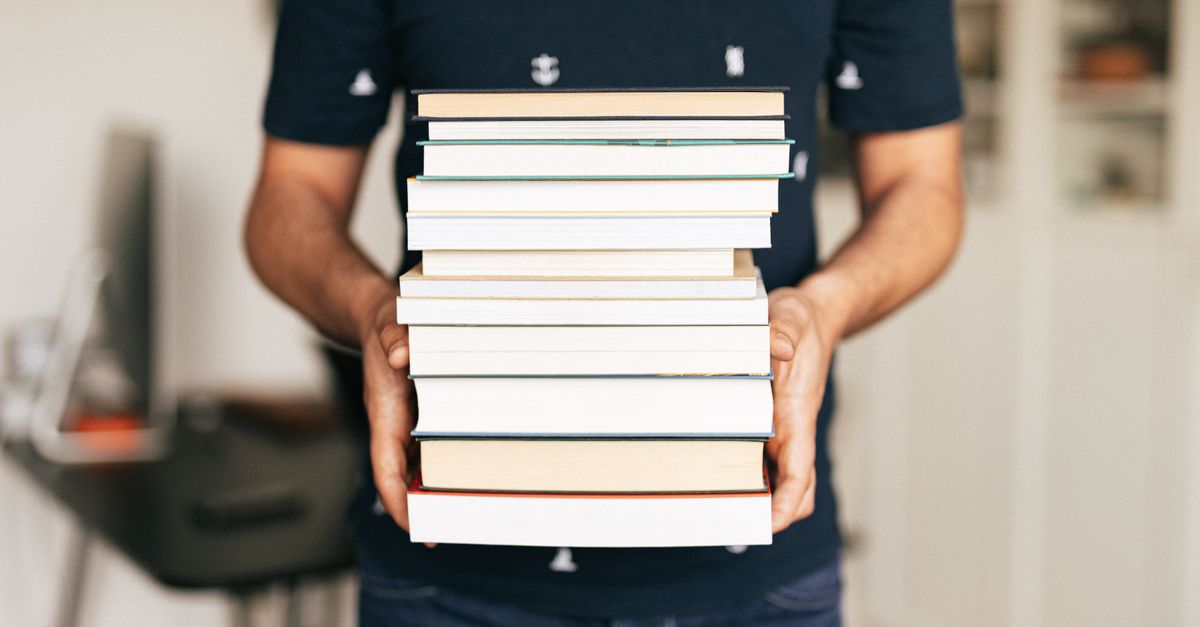 A person holding a stack of books indoors, capturing the essence of knowledge and learning.